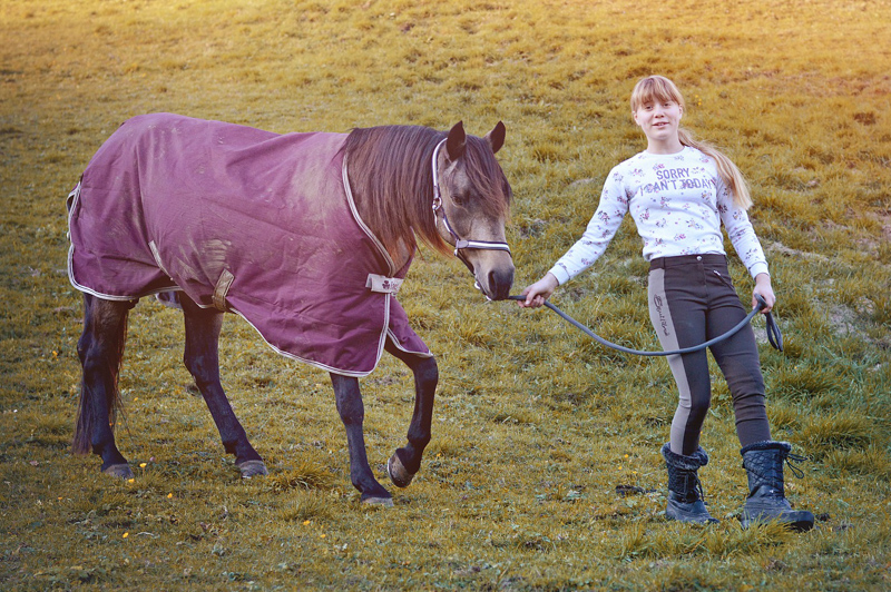 Mädchen führt Pferd mit Abschwitzdecke auf der Wiese